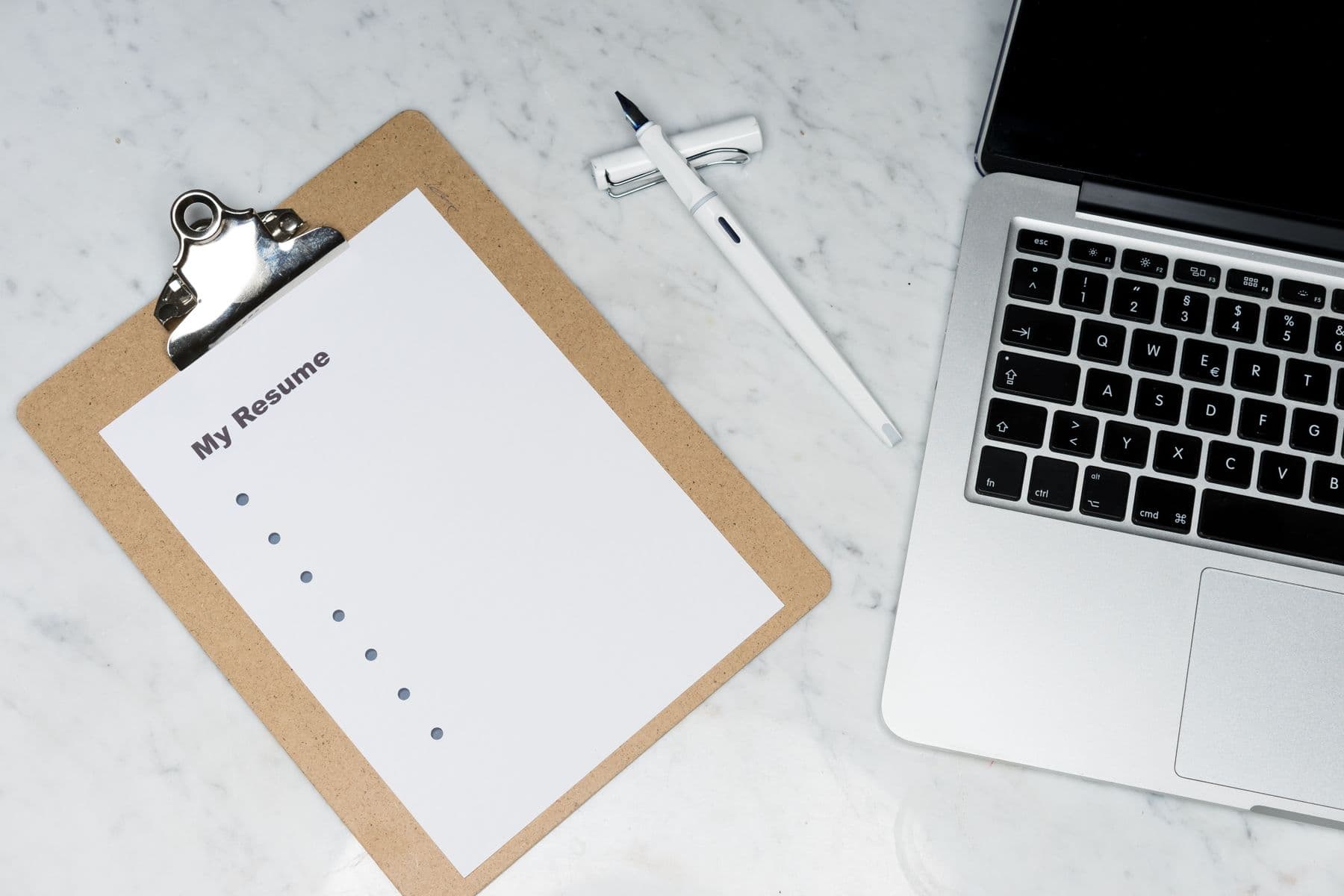A résumé on a clipboard beside a laptop and pen